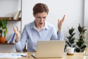 Annoyed angry businesswoman looking at laptop frustrated about broken computer